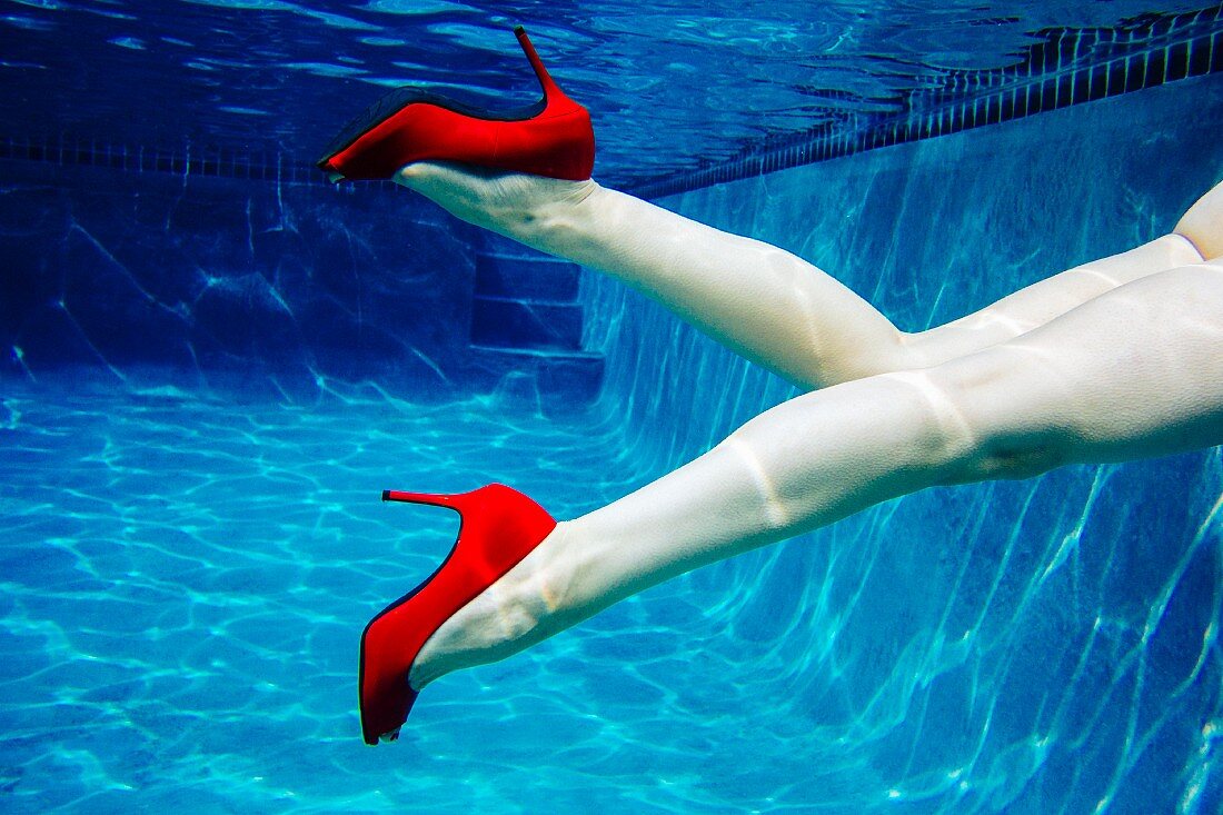 Frauenbeine mit roten High Heels unter Wasser im Swimmingpool