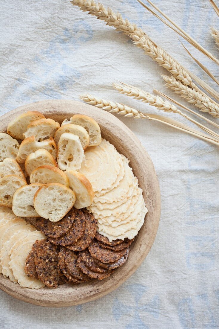 Various wheat crackers sitting in a stoneware bowl next to dried wheat ears