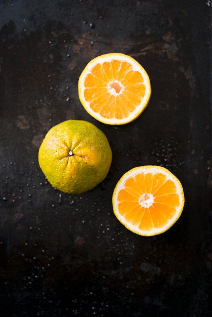 Ugli fruit, whole and halved, on a black surface