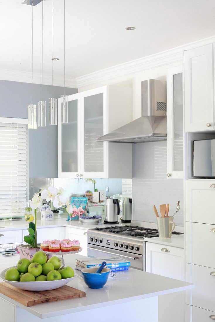 Bowl of apples on island counter in modern fitted kitchen with white fronts