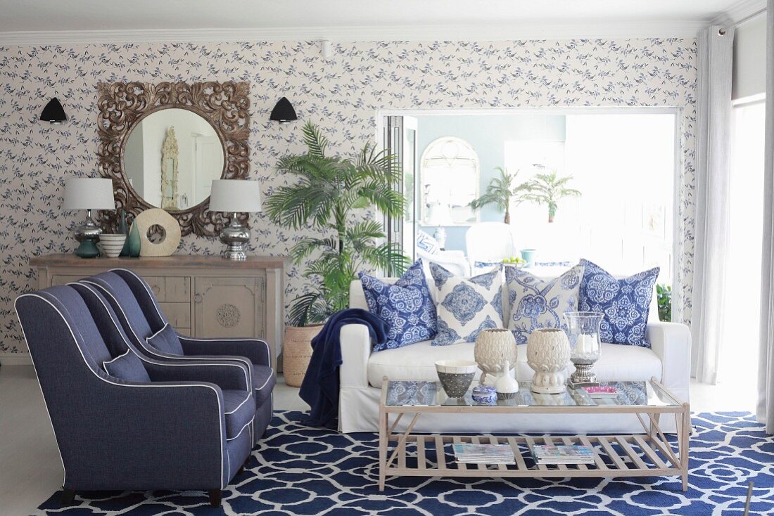 Blue and white living room with mixture of patterns on wallpaper, cushions and rug