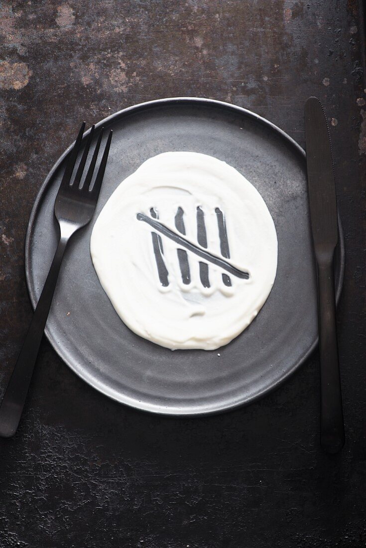 A grey plate with cutlery and a dollop of yoghurt with five tally marks
