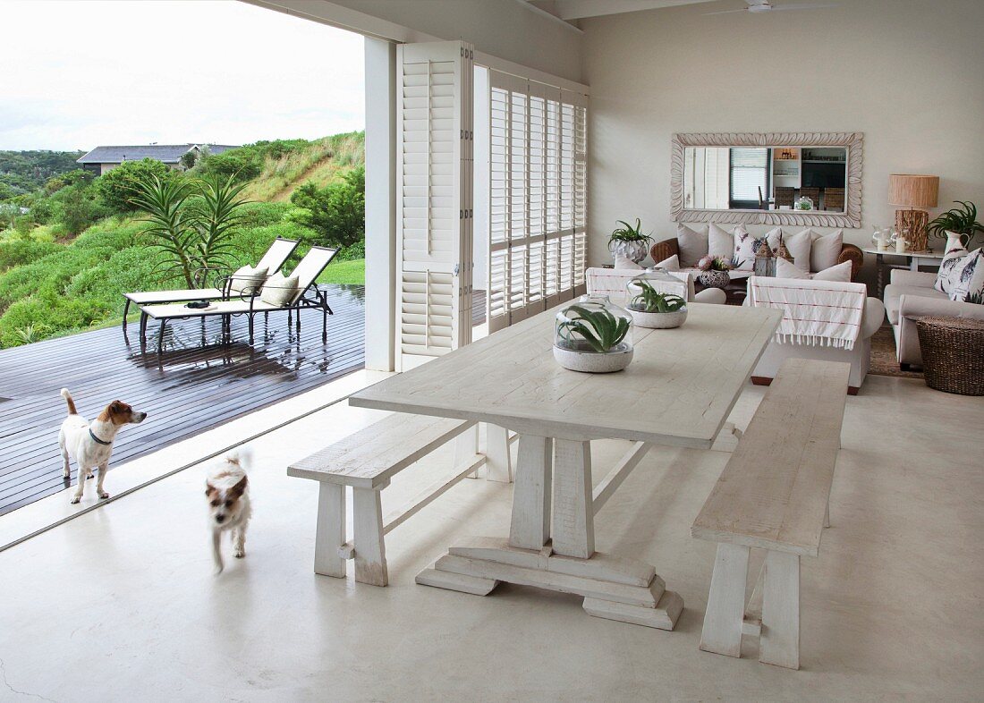 Rustic dining table and wooden benches next to sliding folding doors leading to terrace