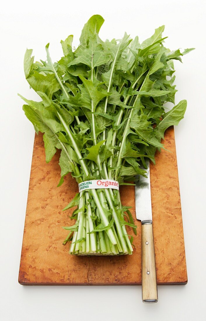 Organic dandelion leaves on a chopping board with a knife