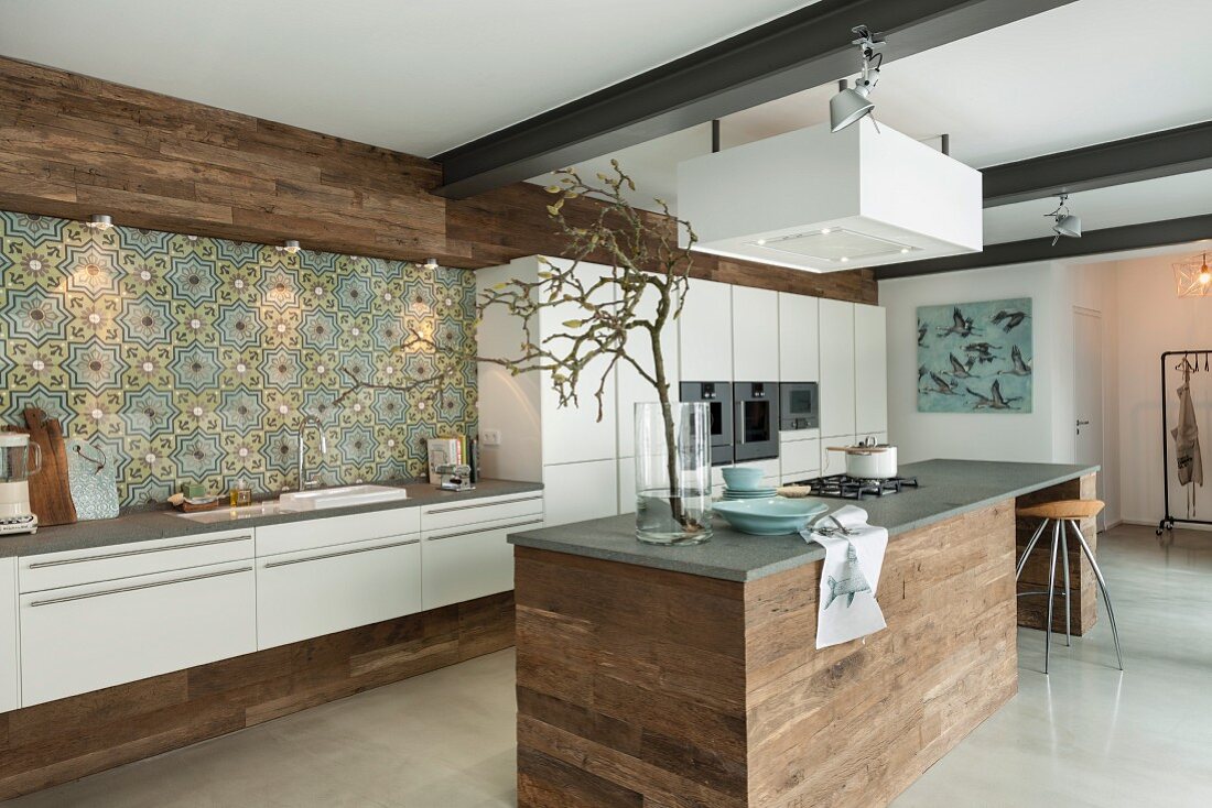 A modern, open-plan kitchen with Mediterranean-style wall tiles and an island counter clad with raw wood