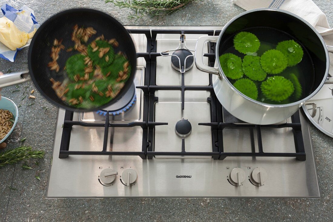 A modern gas stove set in a natural stone work surface with food being prepared in a pot and a pan