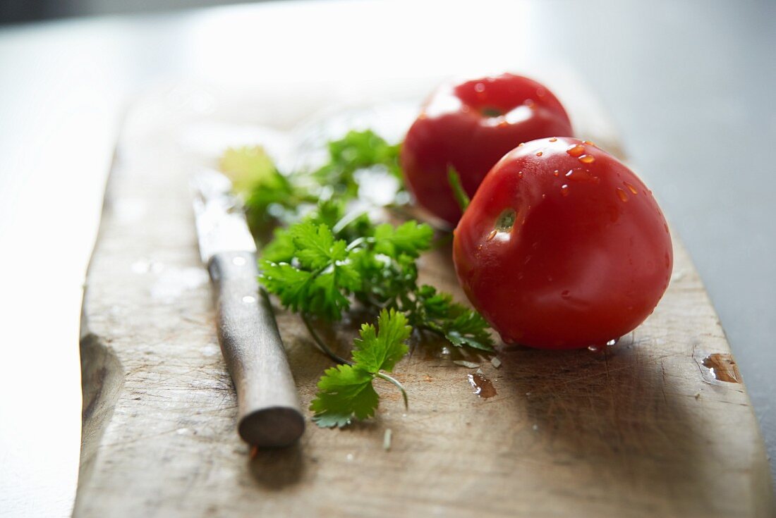 Frische Tomaten und Koriandergrün auf Schneidebrett mit Messer