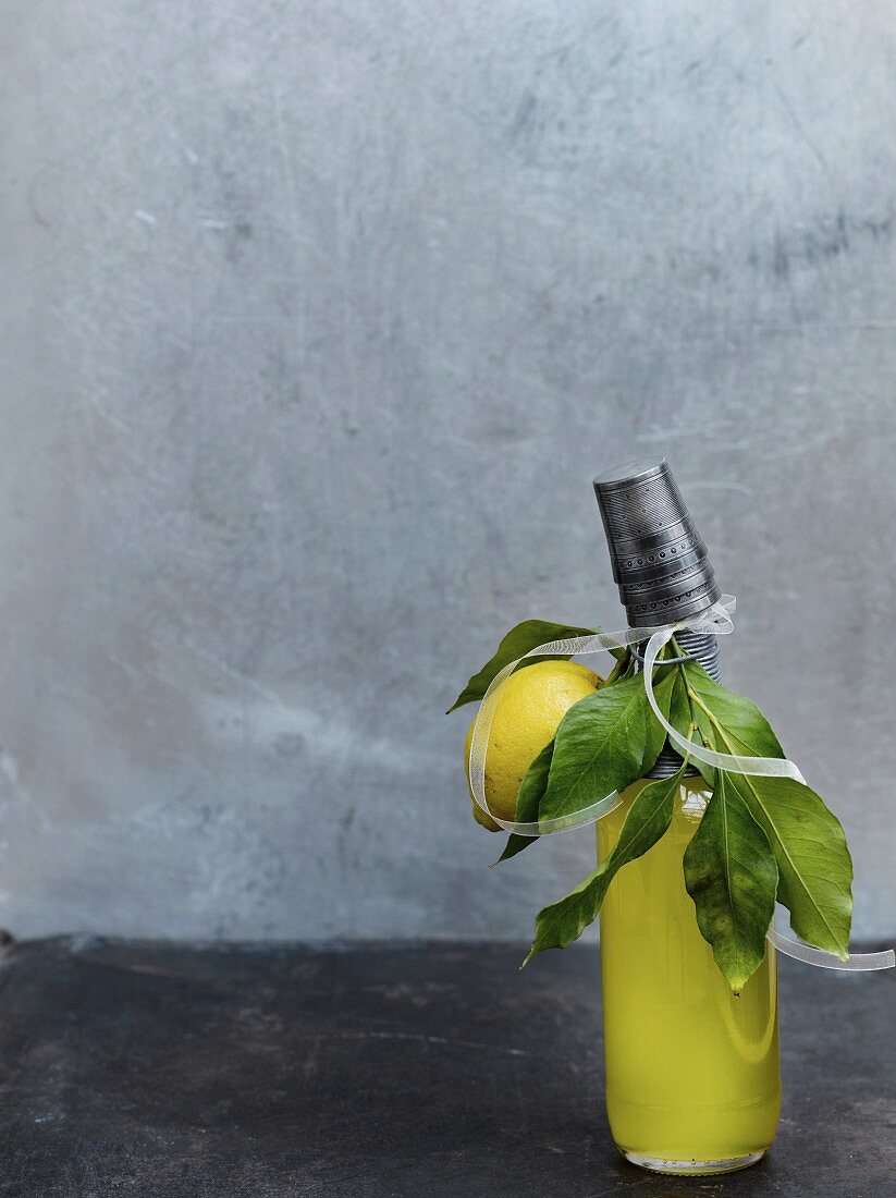Selbstgemachter Zitronenlikör in Flasche dekoriert mit Zitrone & Blättern