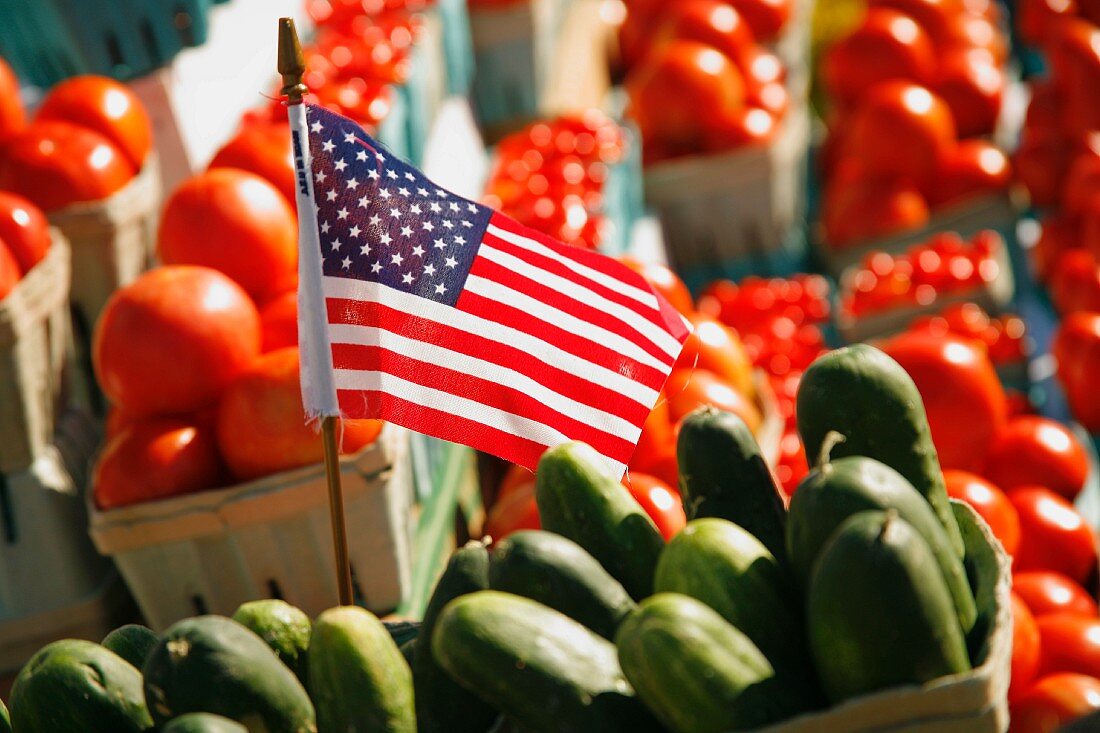 An American flag between cucumbers and tomatoes at a farmers market