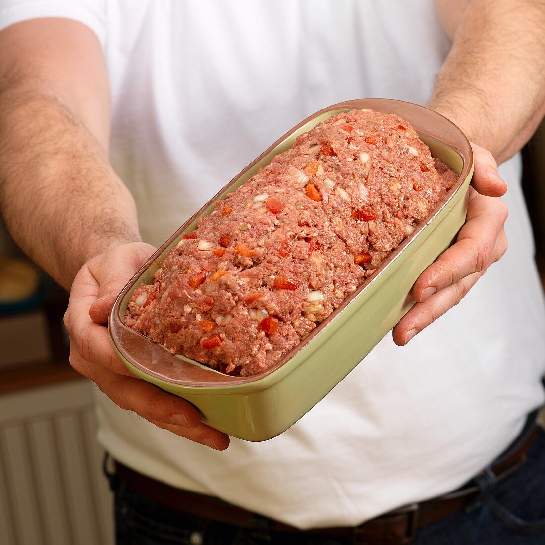 Hands holding raw Mexican meat loaf in green ceramic baking dish