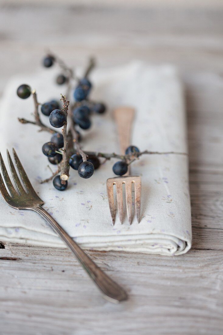 Silver forks and a napkin decorated with a sprig of sloes