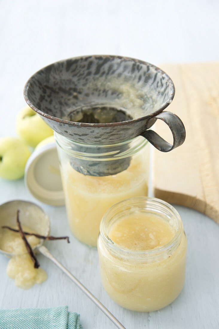 Homemade apple sauce being transferred to a jar with a funnel
