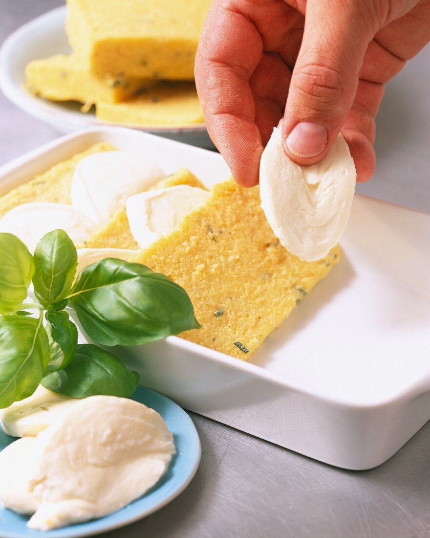 Cold polenta and mozzarella being layered in a baking dish