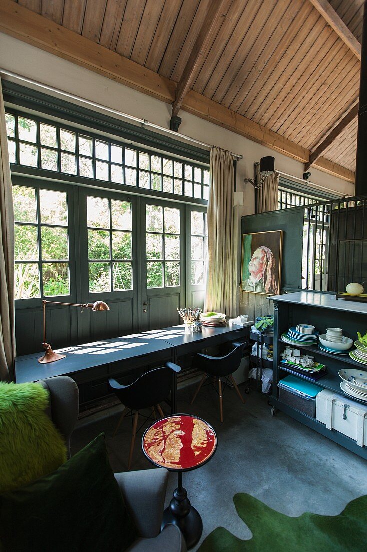 Table, shell chairs and crockery on sideboard in converted stables with wooden ceiling and doors