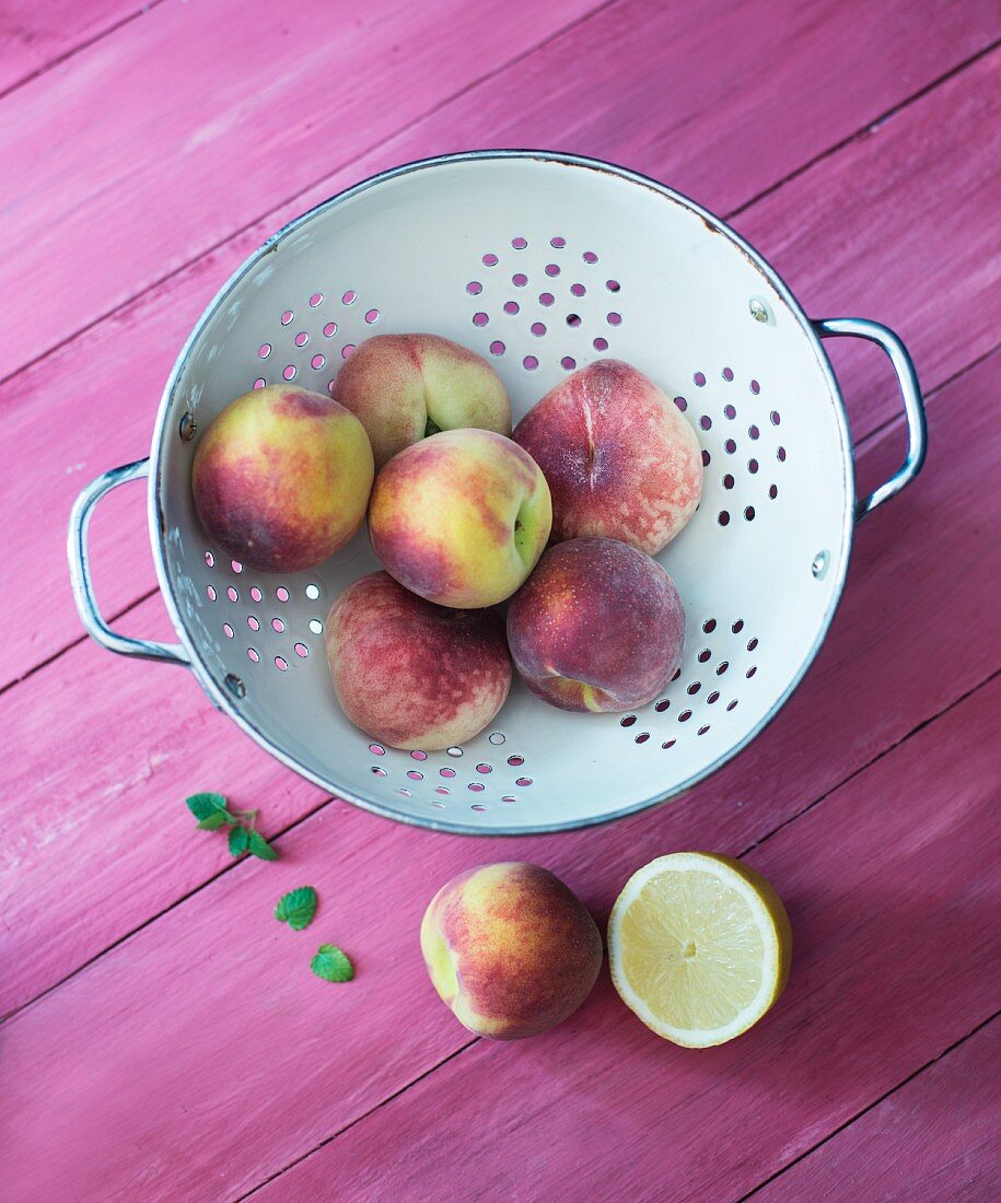 Pfirsiche und Weinbergpfirsiche im Küchensieb, Minze und Zitrone
