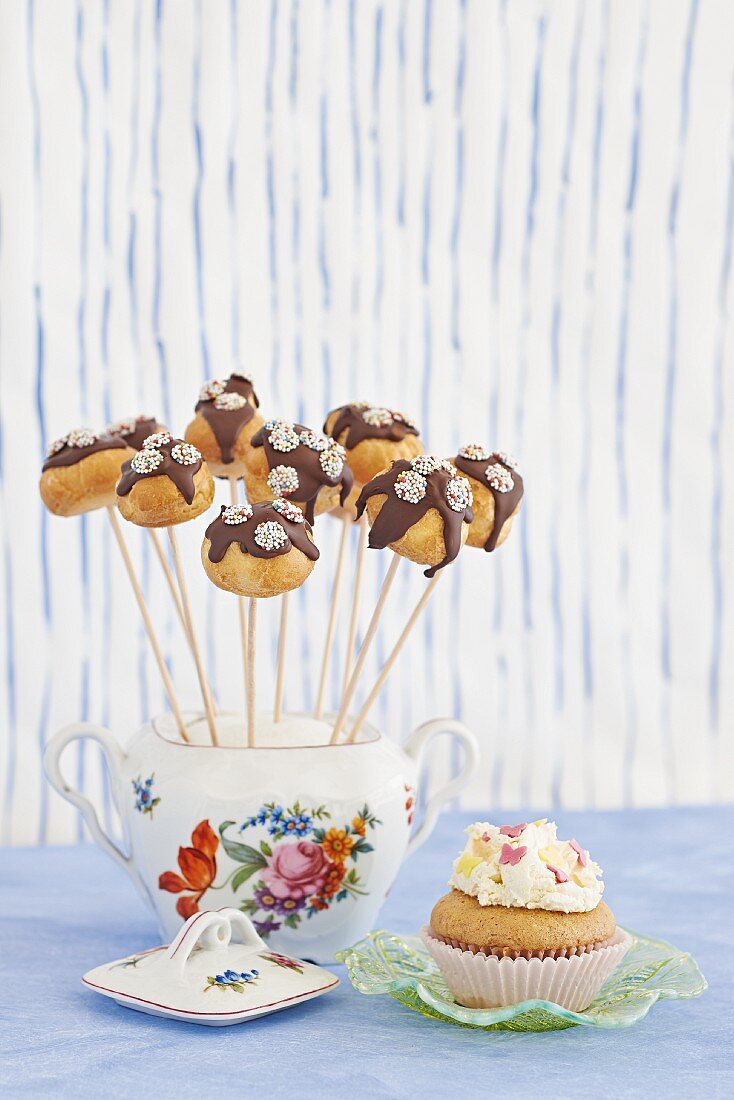 Cake pops stood in vintage sugar bowl next to cupcake