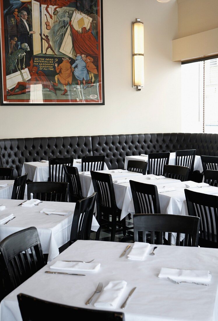 A restaurant dining room with tables laid with white tablecloths and black chairs