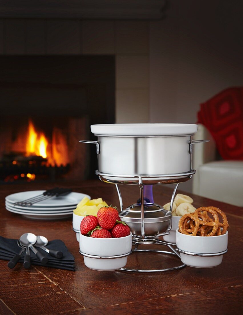 Chocolate fondue with strawberries, banana, pineapple and pretzels in front of a fire