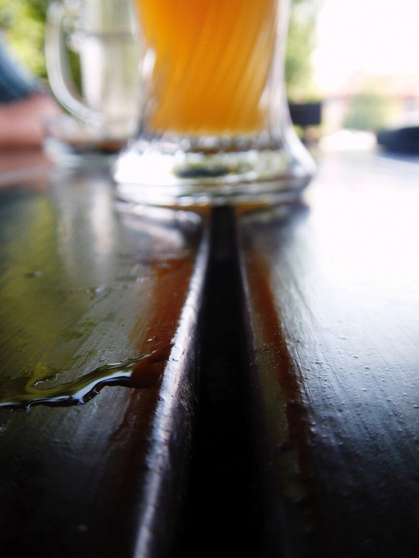 A glass of lager and drops of water on a wooden table