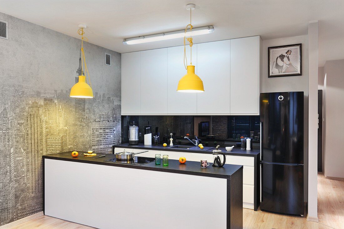 Open-plan fitted kitchen with yellow pendant lamps and photo wall mural of New York skyline in pale grey