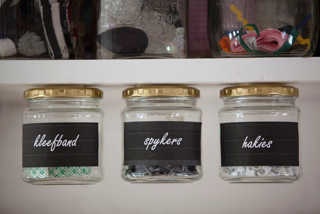 Labelled storage jars with lids attached to bottom of shelf by magnets