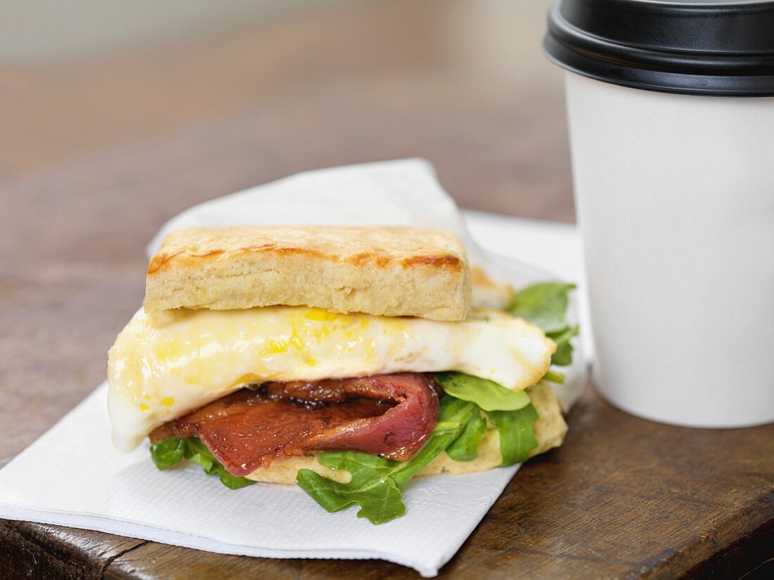 A bacon and fried egg sandwich with a coffee to go