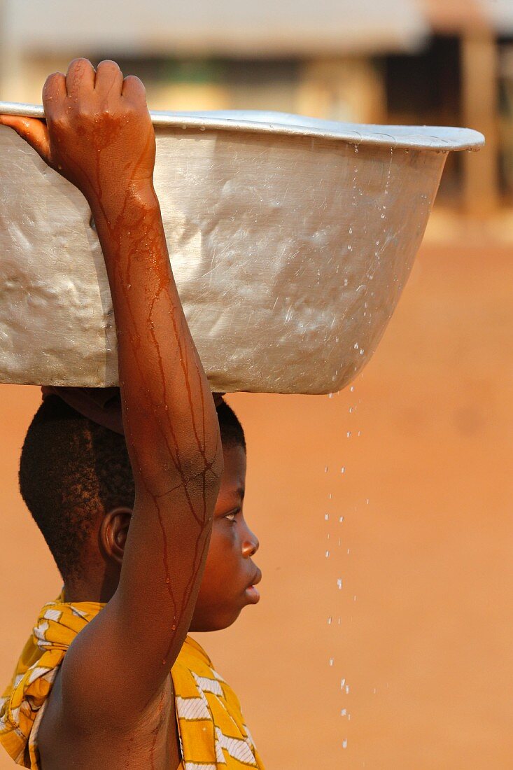 A child carrying a bowl of water on his head in an African village, Togo, West Africa