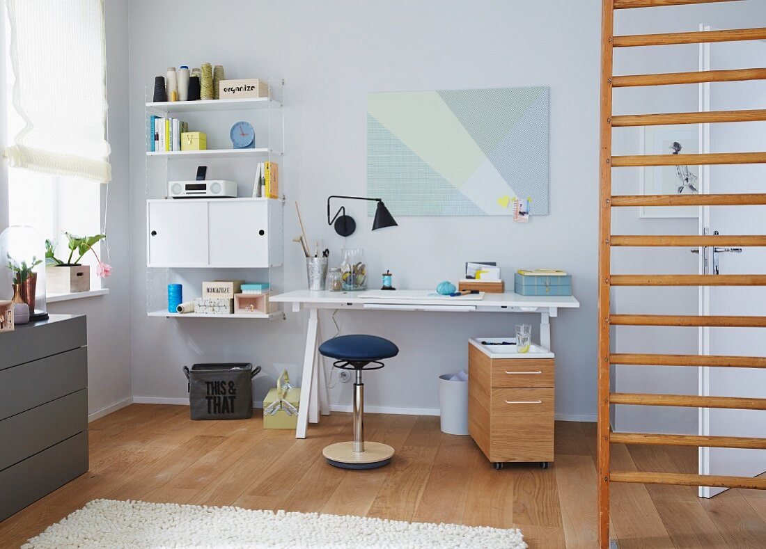 An office corner with a height-adjustable desk and an ergonomic swivel chair with a ladder wall to the side