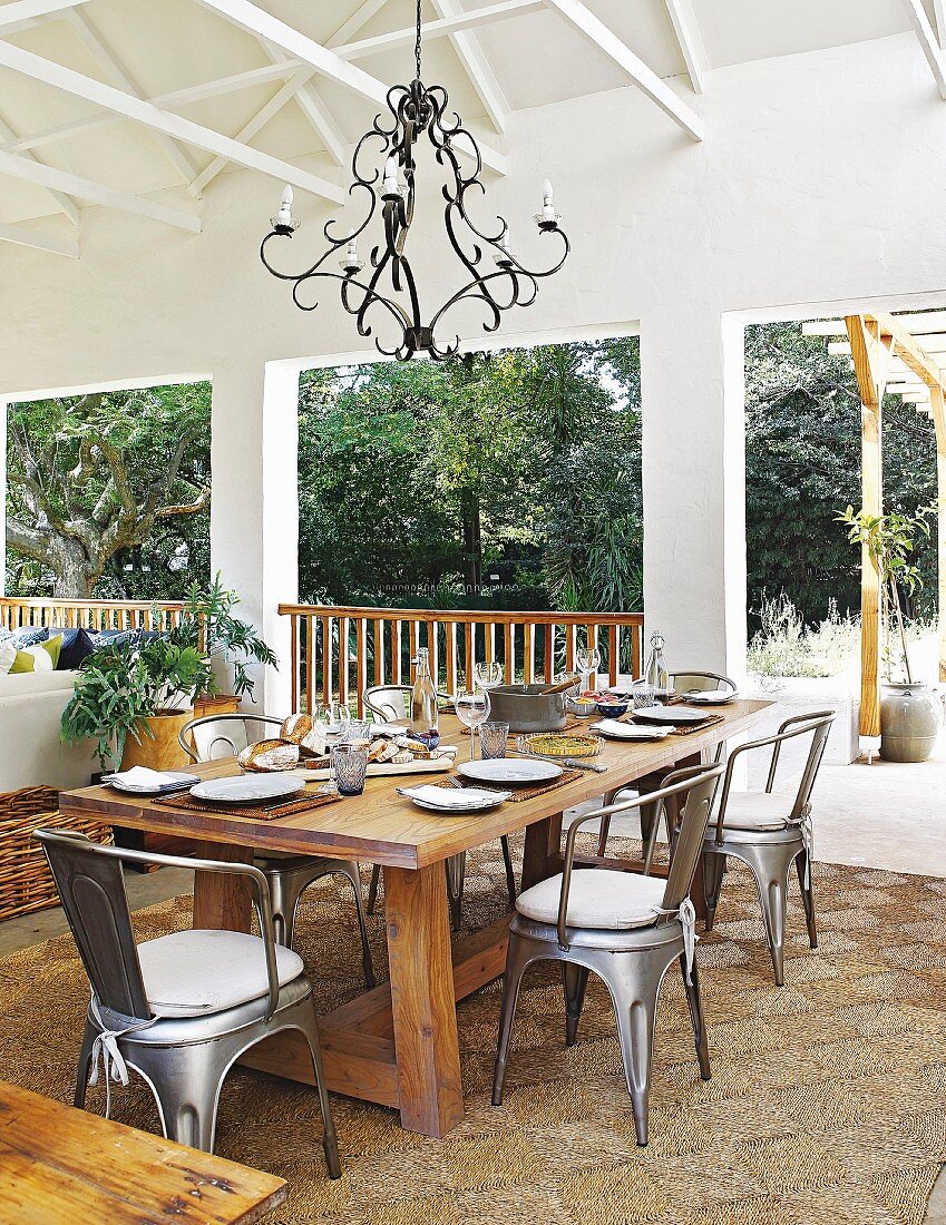 Überdachte Terrasse in Brauntönen mit großem Esstisch und Metallstühlen im Industriestil