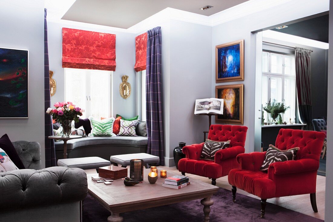 Armchairs with red velvet covers and wooden table in traditional living room with window seat in window bay