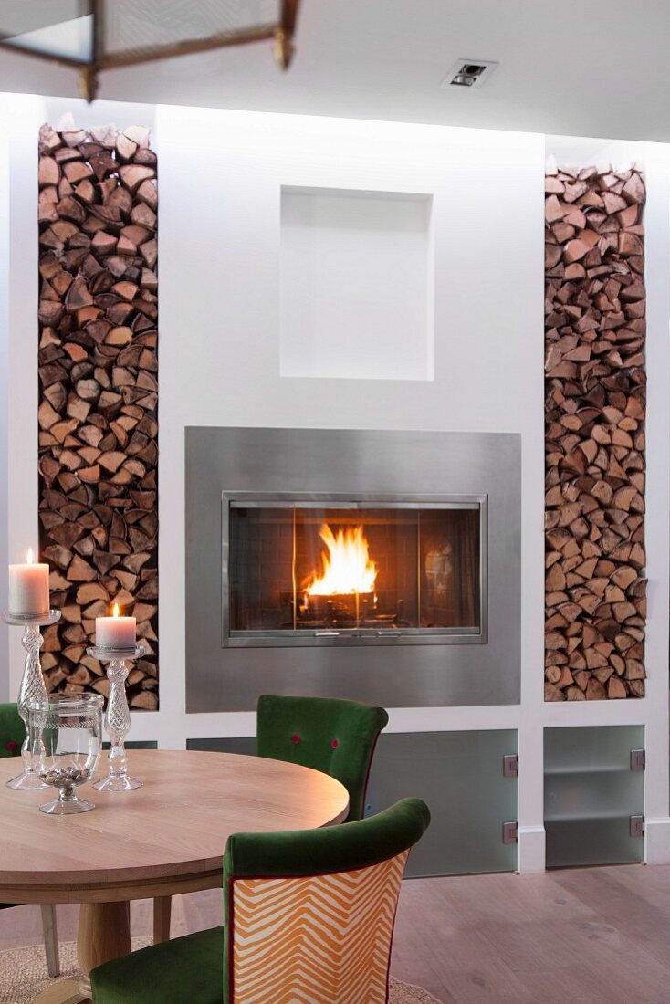 Dining set in front of fire in fireplace flanked by firewood in niches