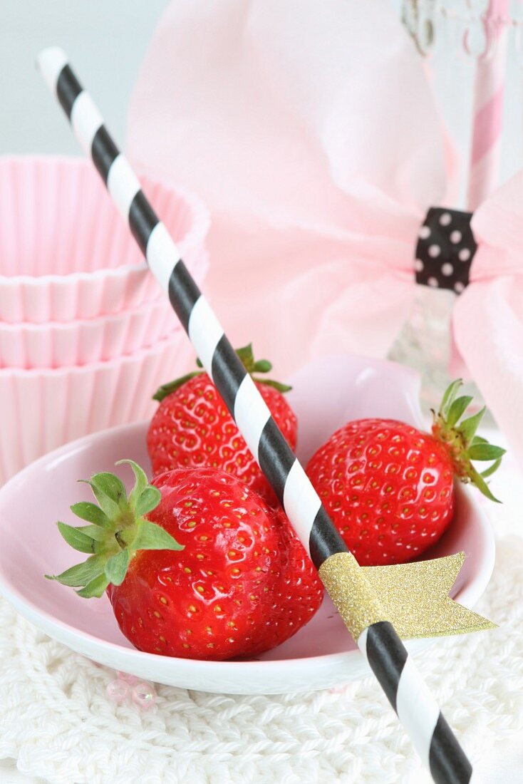An arrangement of fresh strawberries, a straw and cake cases