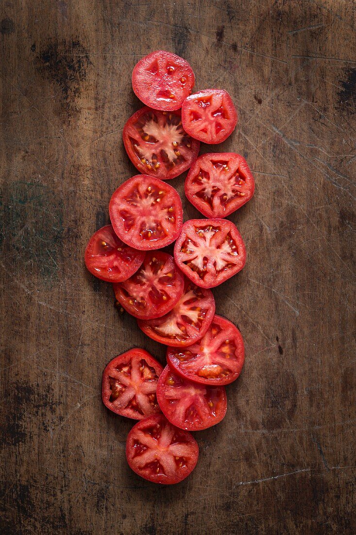 Scheiben von roten Tomaten auf Holzuntergrund (Draufsicht)