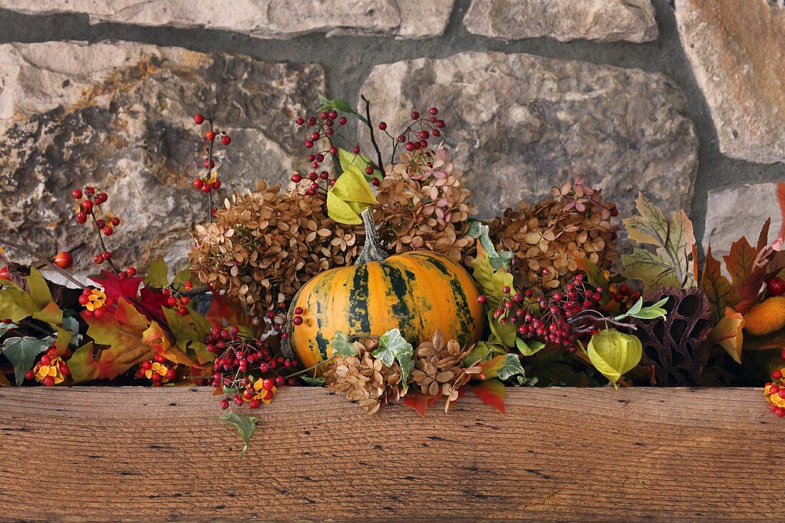 Autumnal arrangement of pumpkin, sprigs of berries and leaves against stone wall