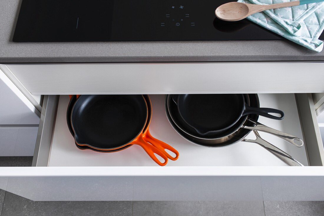 A half-open drawer in a kitchen with a view of various sized pans