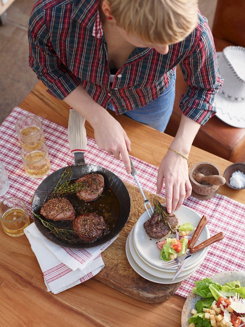 A woman arranging pepper fillet steaks on plates