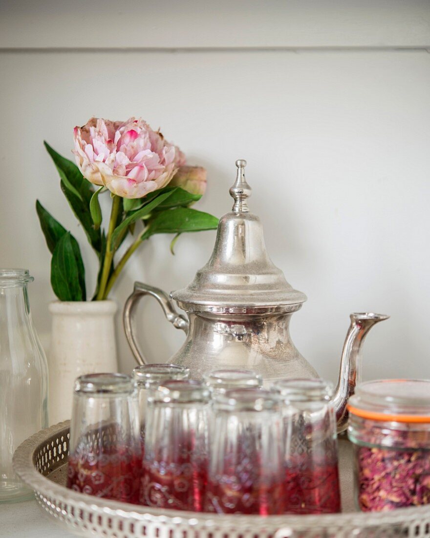 Silberne Teekanne auf Tablett mit orientalischen Teegläsern und Pfingstrose in Vase