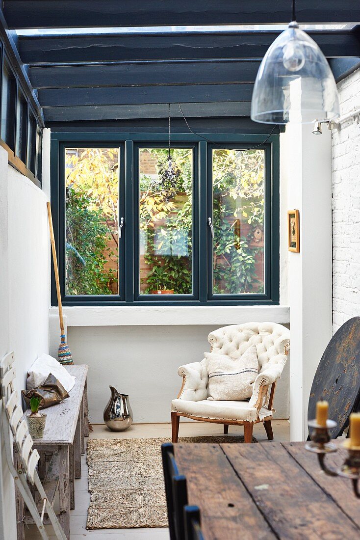 Rustic chair, antique armchair and wooden bench in extension with wood-beamed ceiling and windows