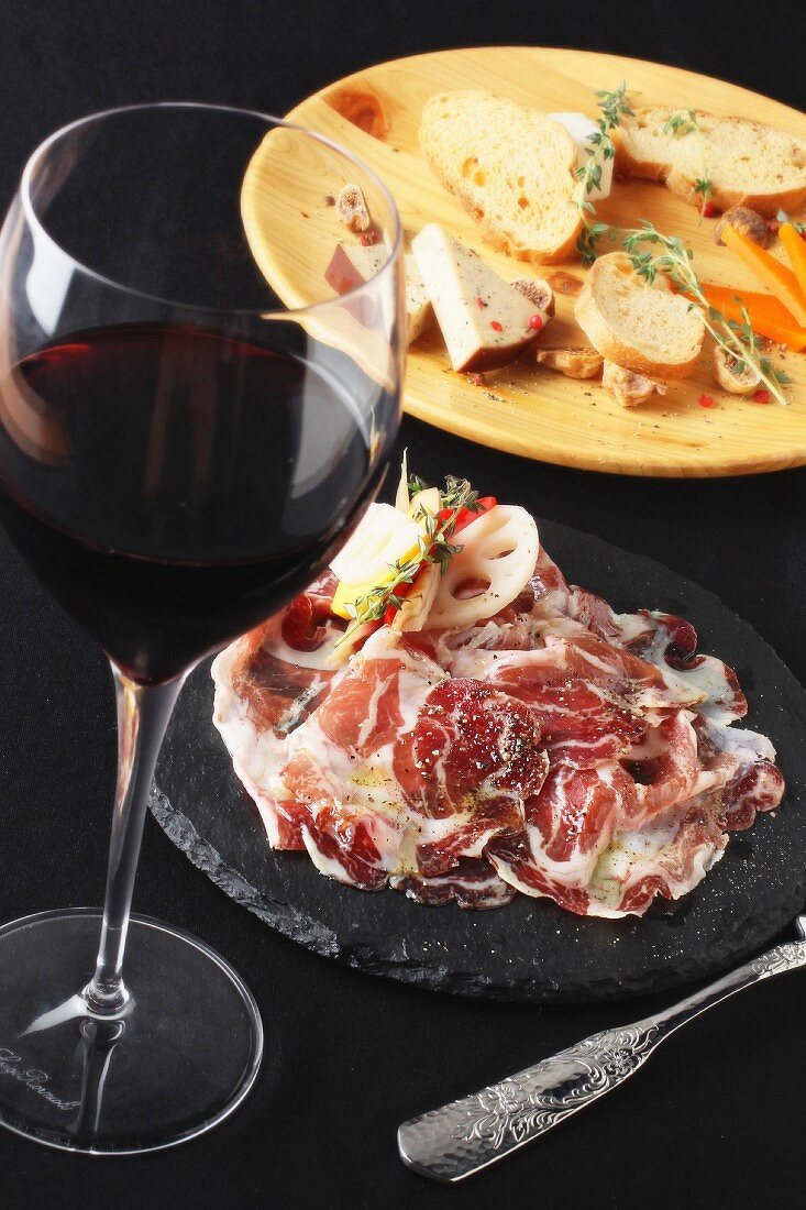 An appetiser platter with raw ham and a glass of red wine