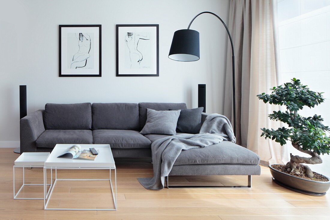 Nest of white coffee tables in front of grey sofa combination, black arc lamp and bonsai tree