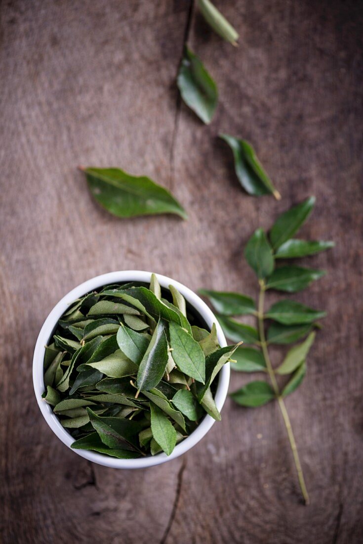 A bowl of curry leaves on a wooden surface