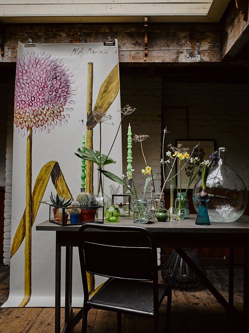 Verschiedene Vasen mit Blumen auf Tisch, im Hintergrund Poster mit Zwiebelblüte-Motiv