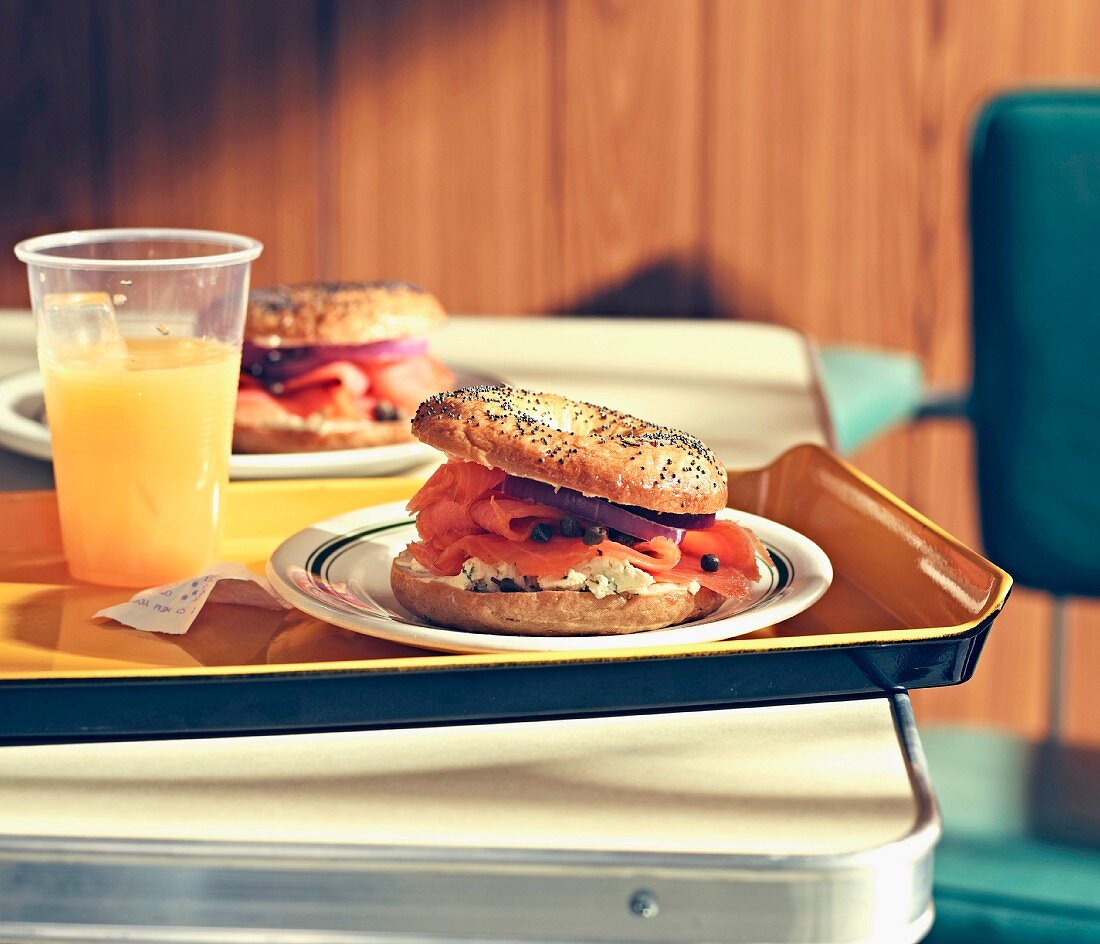 A poppy seed bagel with salmon and cream cheese served with orange juice on a tray in a restaurant