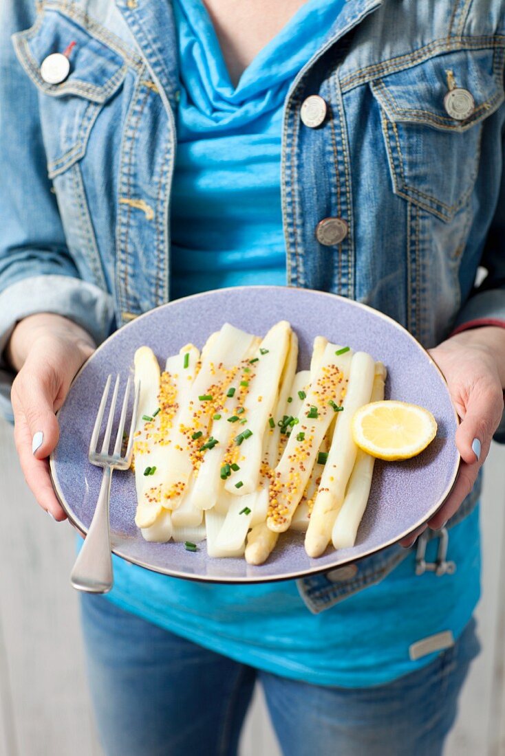 A woman holding a plate of white asparagus with mustard sauce