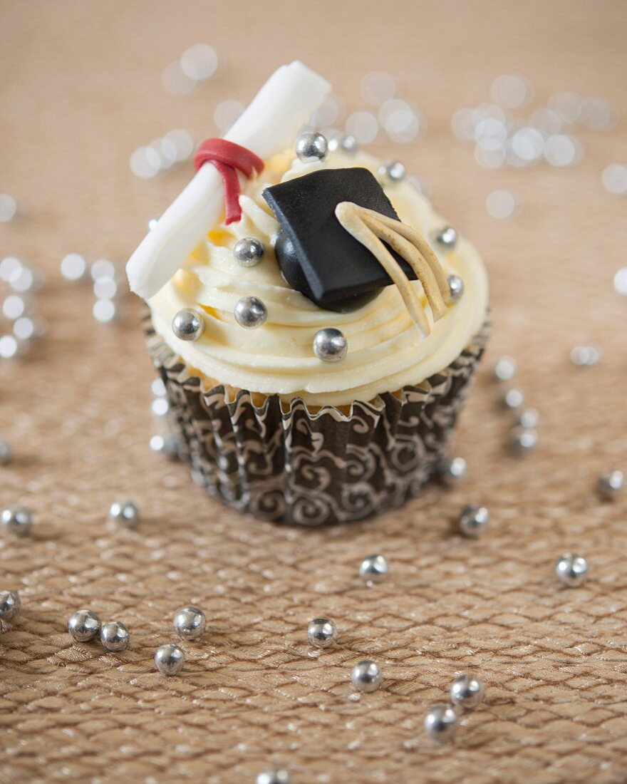 A graduation cupcake decorated with a fondant mortar board and a diploma