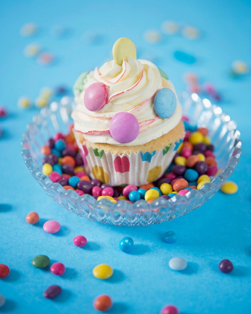 A cupcake decorated with vanilla butter cream and colourful chocolate beans