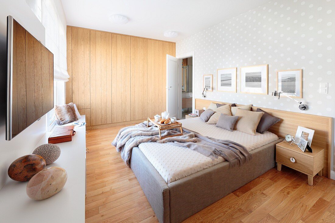 Bedroom with double bed on pale wooden floor and fitted, flat-fronted wooden wardrobes