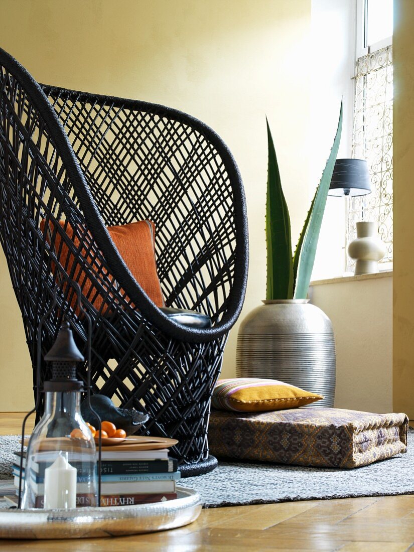 Peacock chair, ethnic floor cushion and agave leaves in African vase