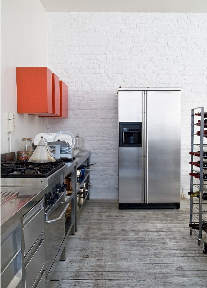 Küchenbereich mit Edelstahl Küchenzeile, oberhalb rot lackierte Hängeschränke, im Hintergrund Kühlschrankkombination