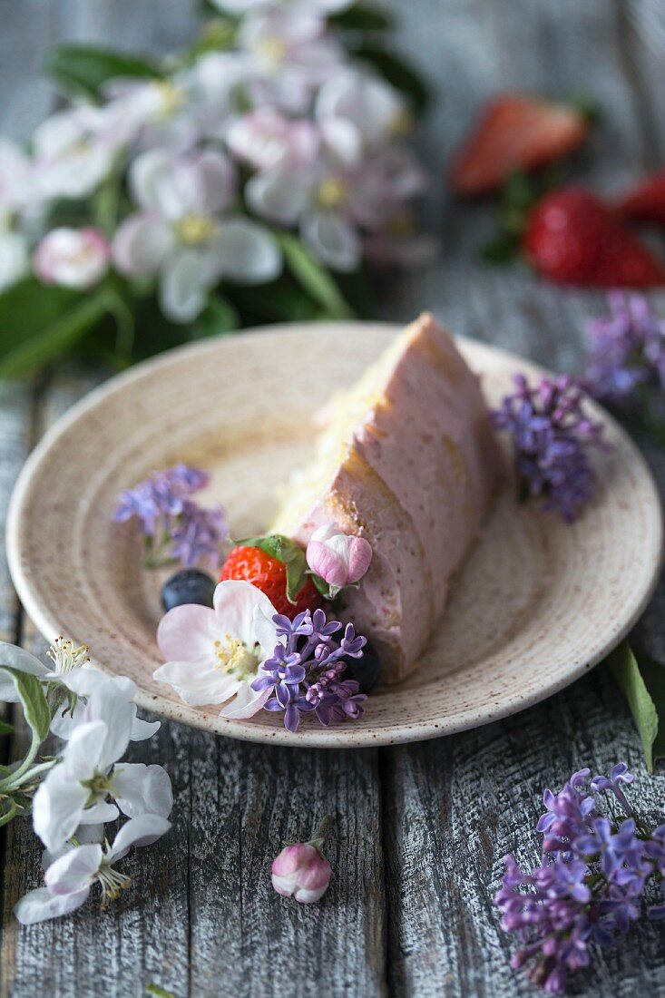 A slice of butter cream cake on a plate decorated with flowers and berries